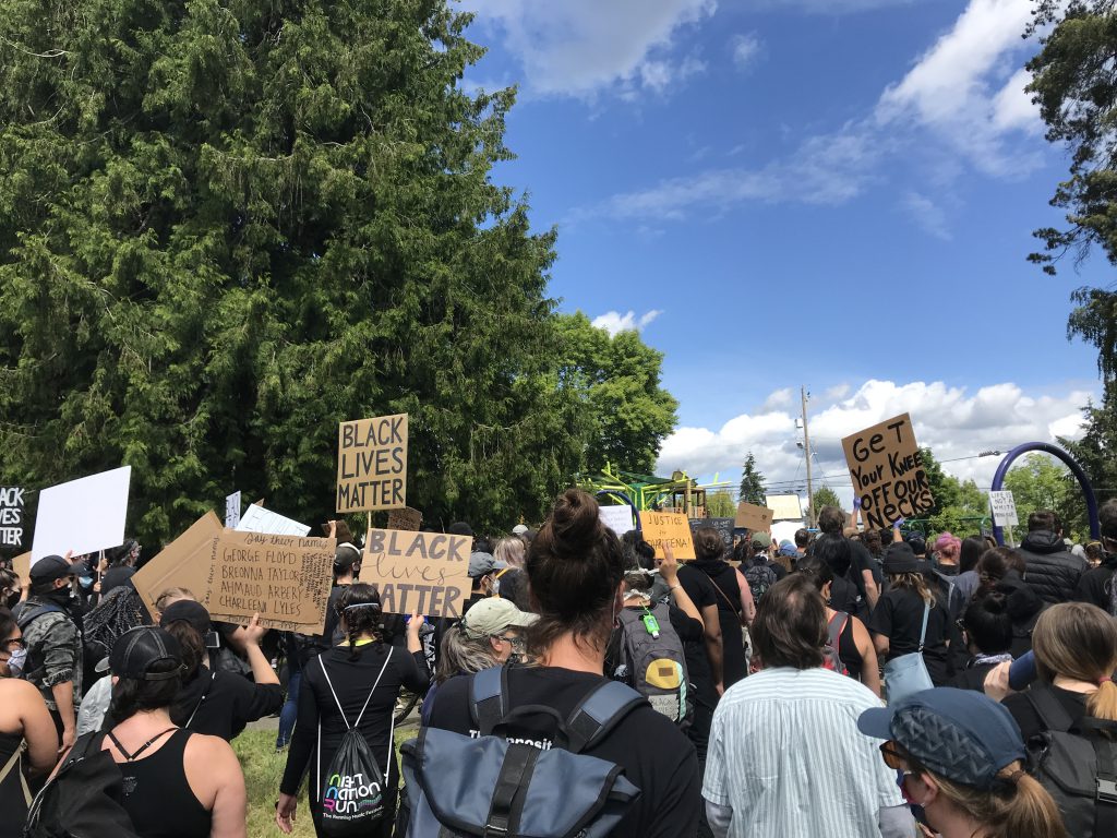 Image of a group of protestors in 2020 with signs that read "Black Lives Matter" and "Get Your Knee off our Necks"