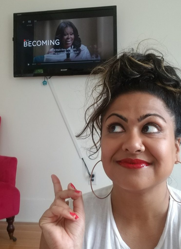 Priya Frank points at the TV featuring Becoming with Michelle Obama