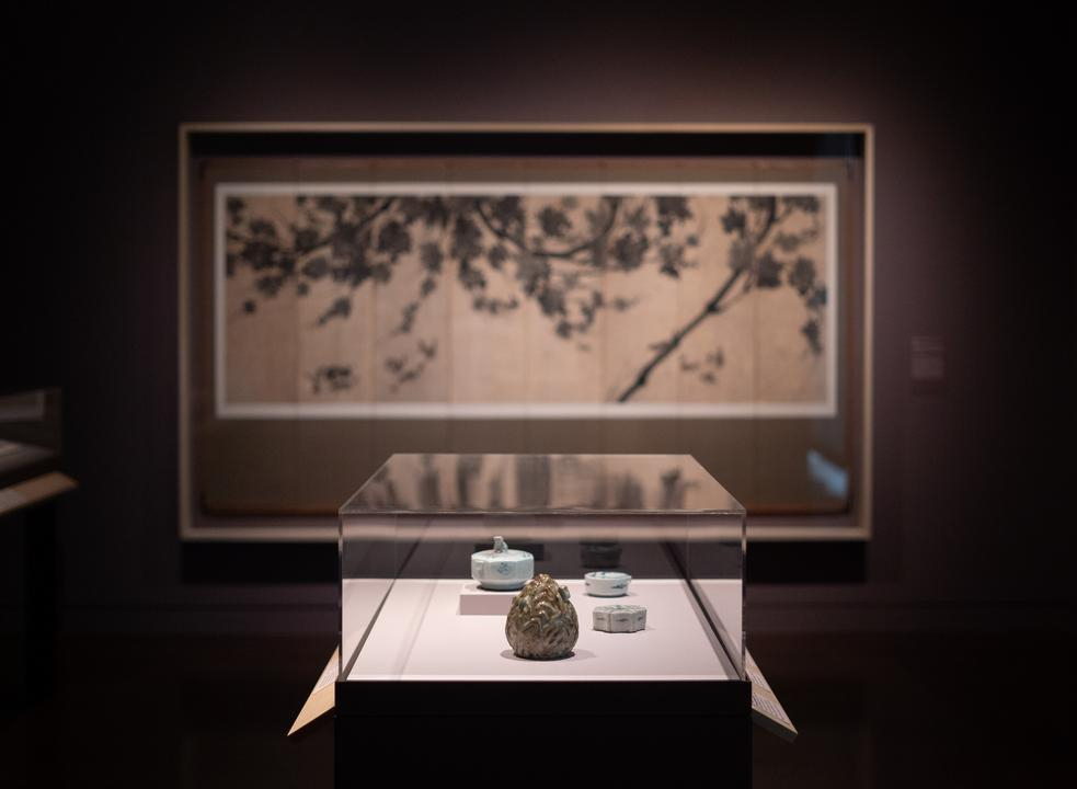 An ink painting in the background and a vitrine with ceramics in the foreground