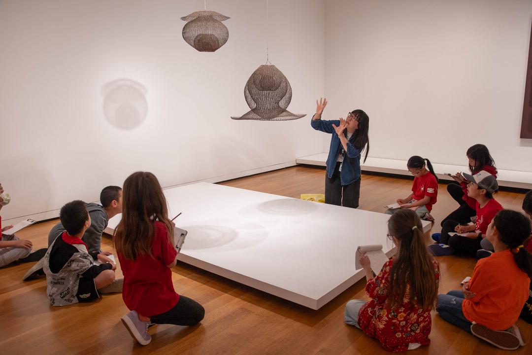 A woman gestures to a sculpture with a group of children on a school tour.