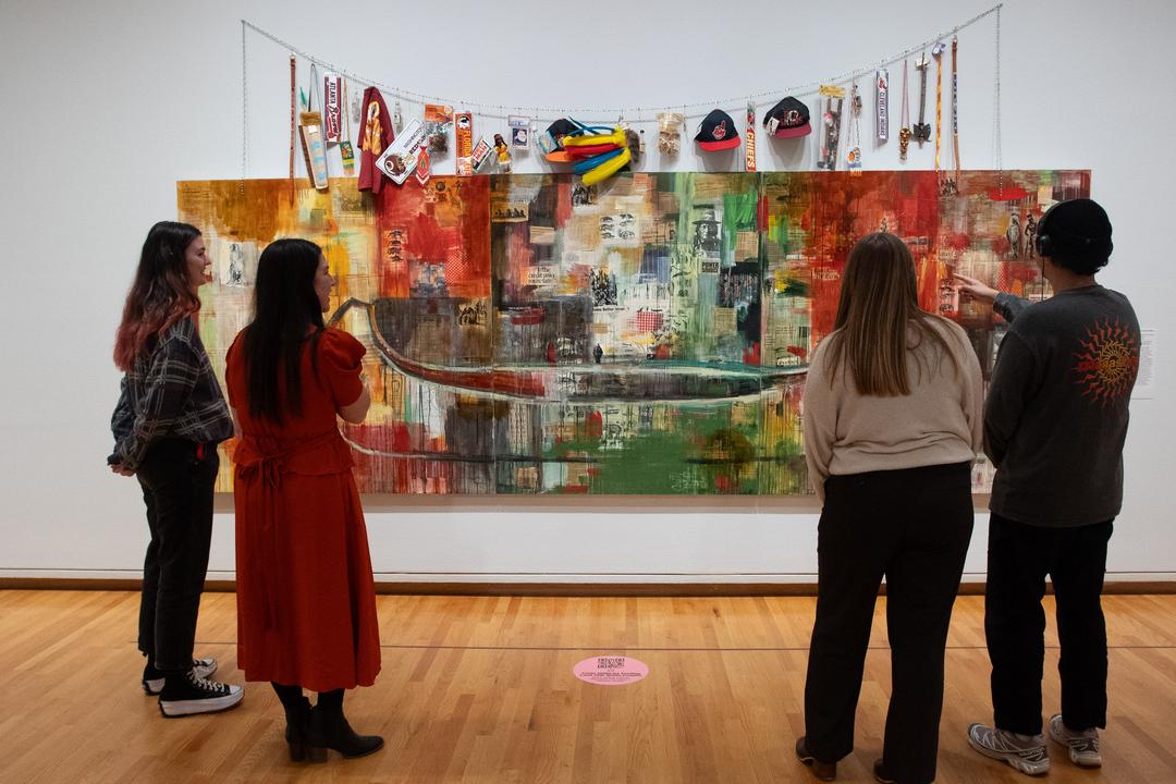 Four people stand in front of a large collage painting.