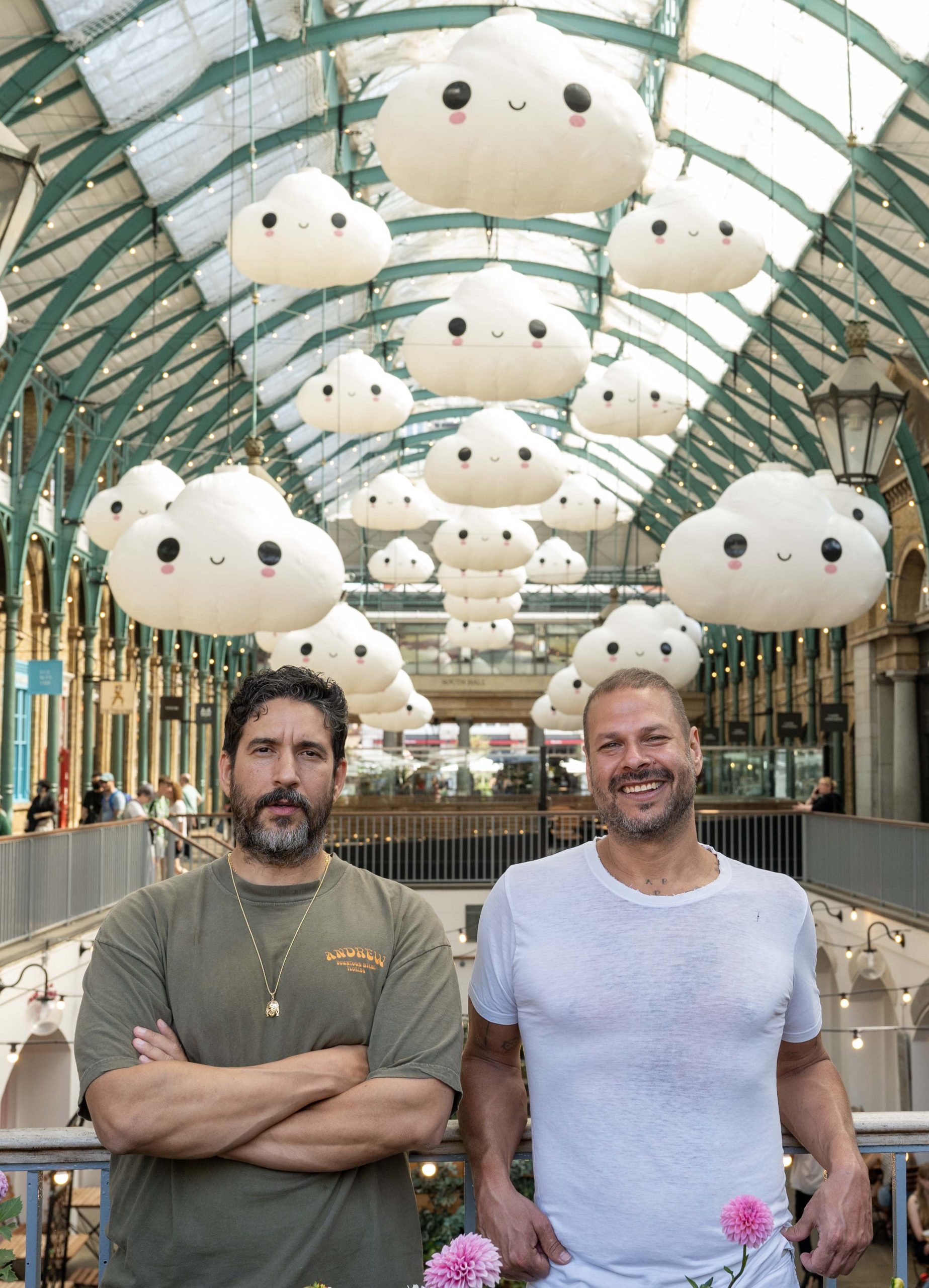 Two men stand in front of an artwork installation of smiling cloud lanterns in a building.