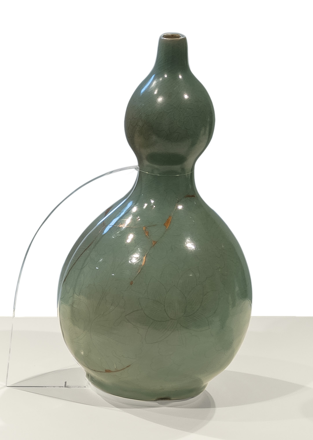 A celadon gourd-shaped bottle mended with golden cracks. Delicate floral motifs of lotus are incised on its surface