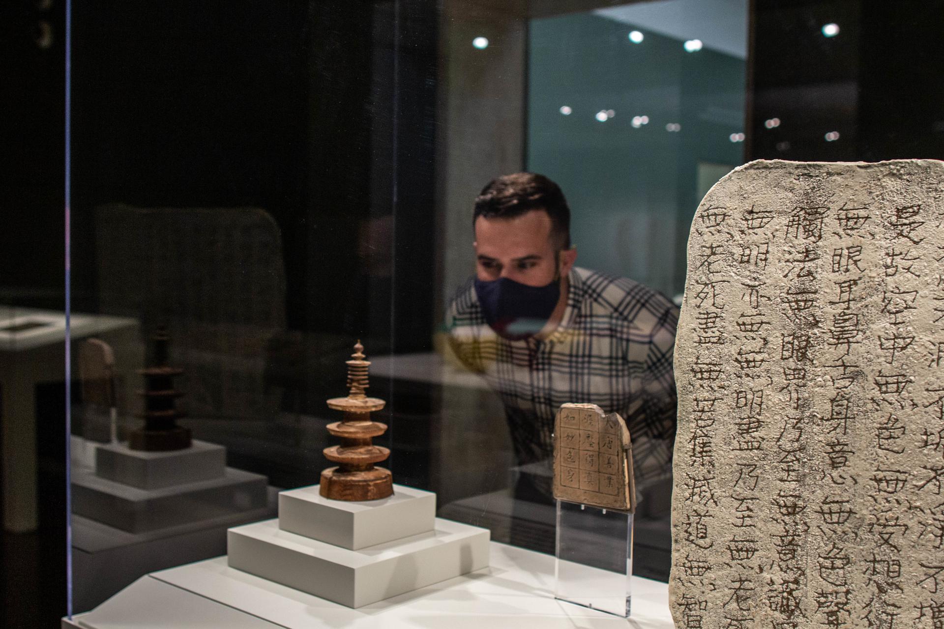 Image of a person wearing a mask looking at a lit paper sculpture installation by Barbara Earl Thomas
